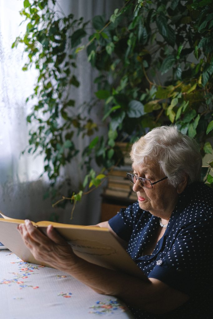 Older woman reading at home beside green plants